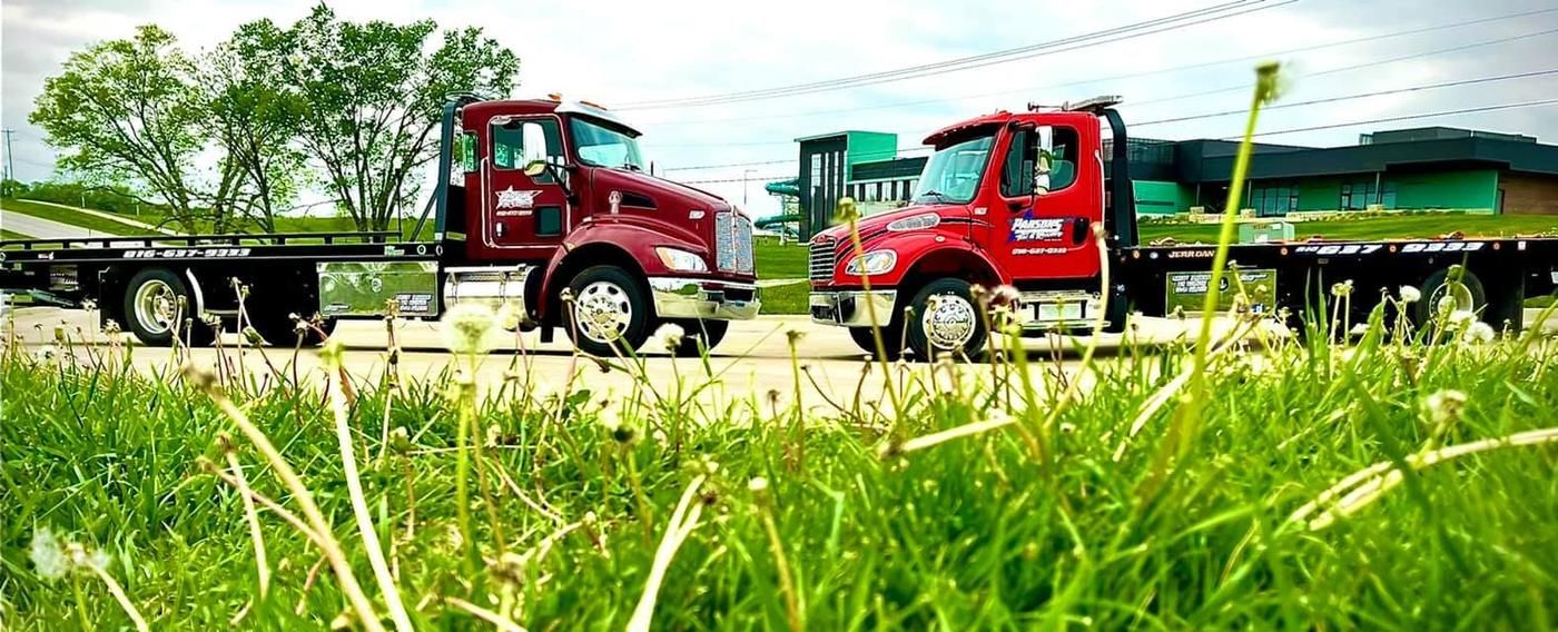 Two Parsons flatbed tow trucks parked nose to nose behind wildflower grass